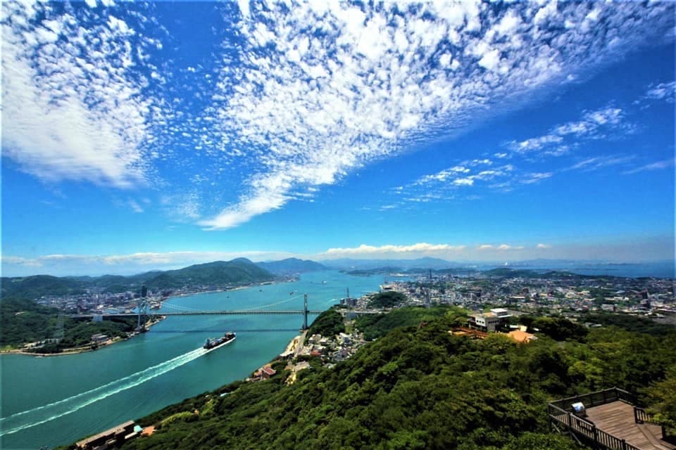 山口県下関市と関門海峡の全景。青い海を大型船が行き交い、関門橋が本州と九州を結ぶ景観。