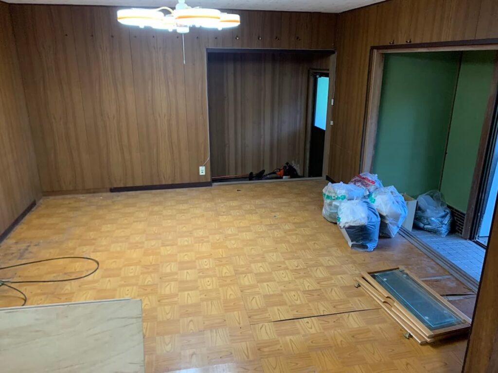 古民家の客室。木目調の壁と照明があり、床には荷物やゴミ袋が置かれた改修前の様子