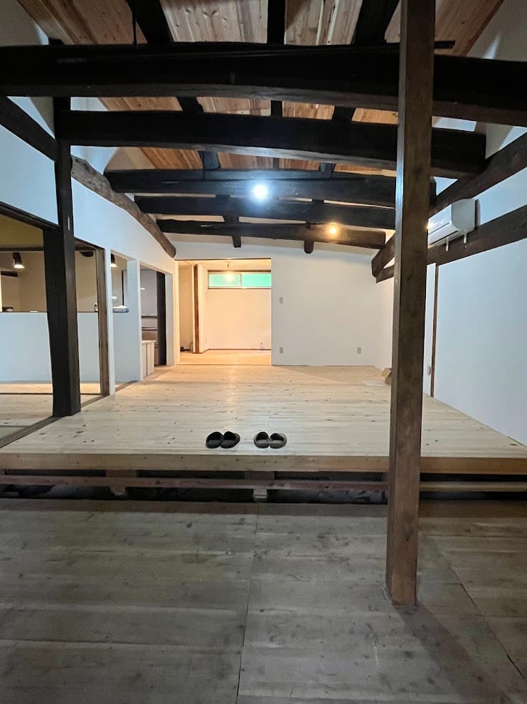 天井を抜き、梁を見せて開放的に仕上げた古民家の居間。白壁と木の床が調和する明るい空間。