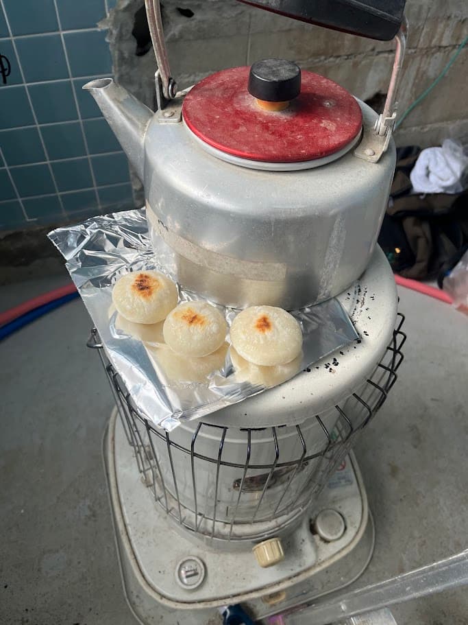 石油ストーブで餅を焼きながら冬の古民家改修作業を進める様子