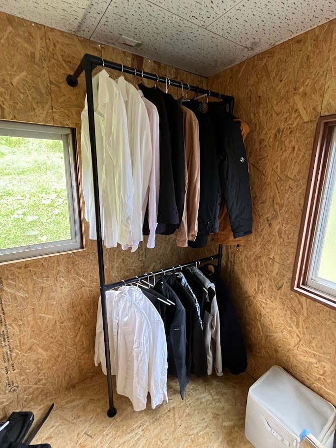 2段式の黒いハンガーパイプに衣類を掛けた管理室の完成状態。シンプルで機能的な空間に。