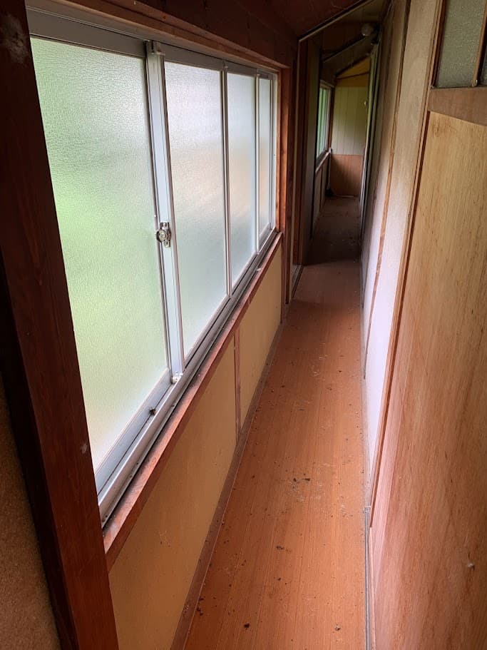 改修前のトイレへ続く廊下。古いアルミサッシと木壁が並ぶ、昭和の雰囲気を残した通路。