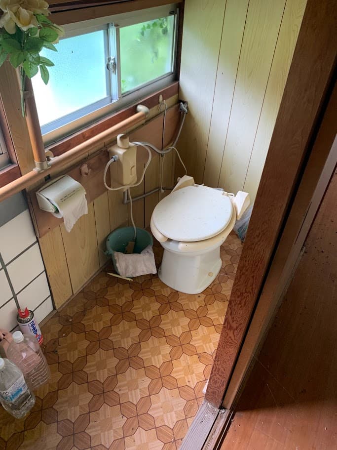 改修前の古いトイレ。木目調の壁とクッションフロアで、経年劣化が見られる和式から洋式に変えられた空間。