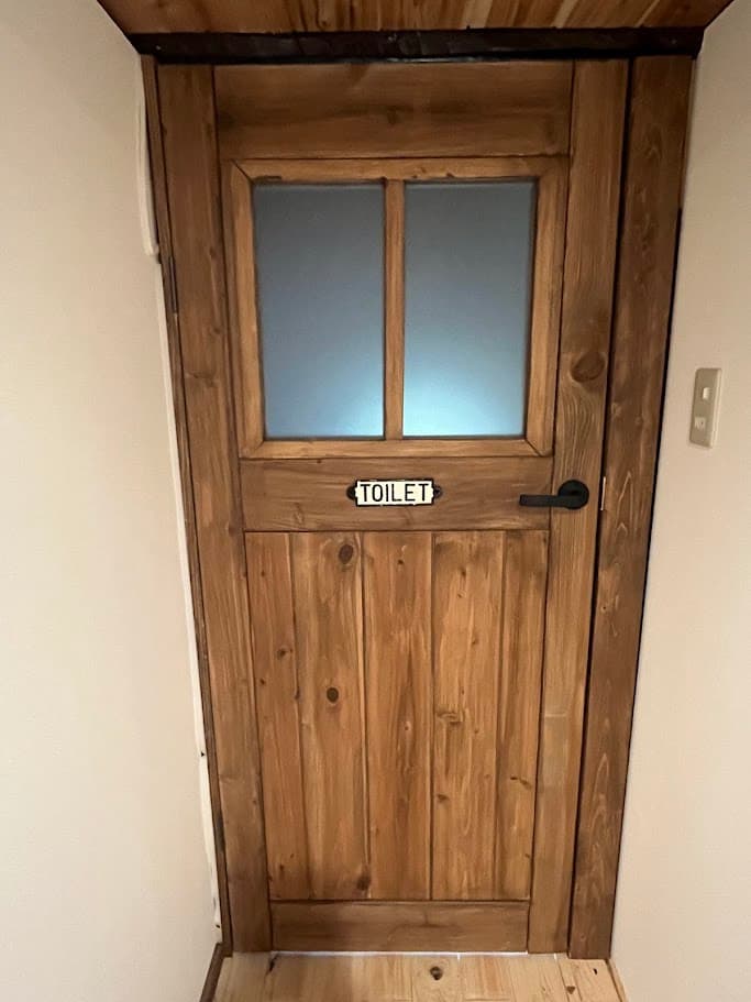 完成した木製トイレドア。ガラス窓付きで「TOILET」のプレートがアクセントになっている。