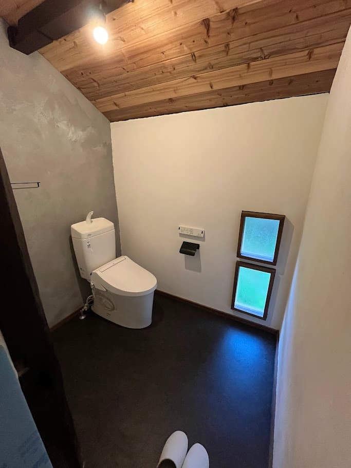改修後のトイレ。白い壁と木の天井、漆喰仕上げの壁が心地よい、古民家らしさを残したモダンな空間。