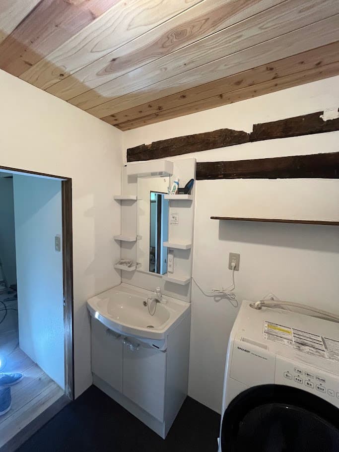 改修後の洗面台周辺。新しい洗面台と洗濯機が並び、梁の意匠を残したデザインが特徴的。