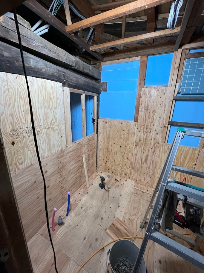 壁の下地を張り替える工程。構造材と断熱材が見える状態で、古民家の骨組みを活かした施工。