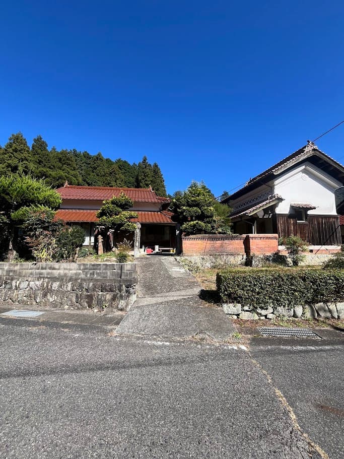 かんぬしの宿となる古民家の外観写真。赤瓦屋根の母屋と白い蔵が写っている。