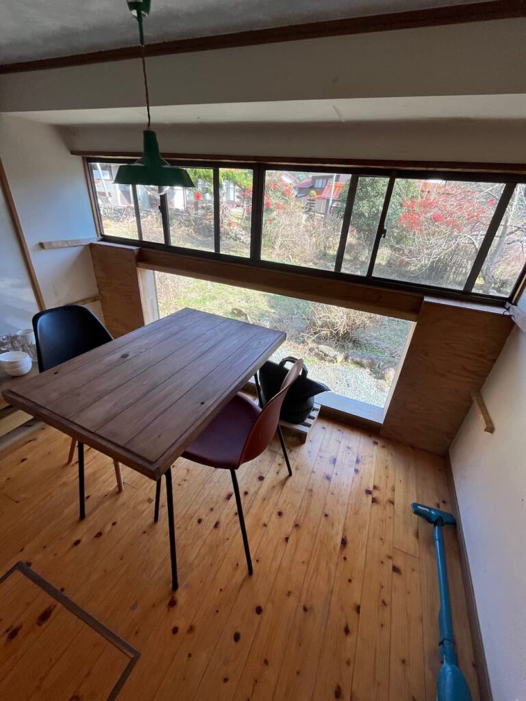 かんぬしの宿の窓際ダイニングスペース。大きな窓から庭を望む木のテーブル席。