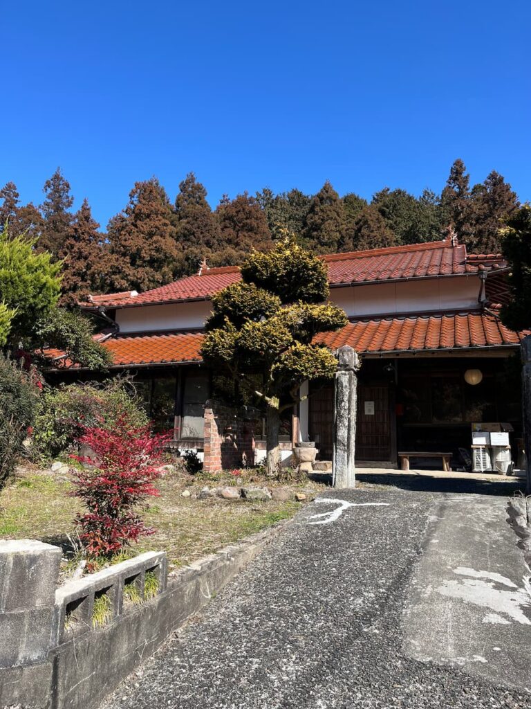 青空の下に佇むかんぬしの宿の外観。赤瓦屋根の古民家。