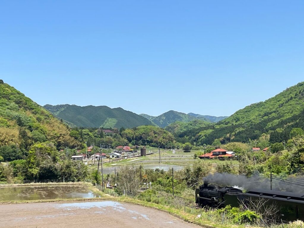 かんぬしの宿周辺の里山風景。山に囲まれた田んぼの中をSL機関車が走っている。
